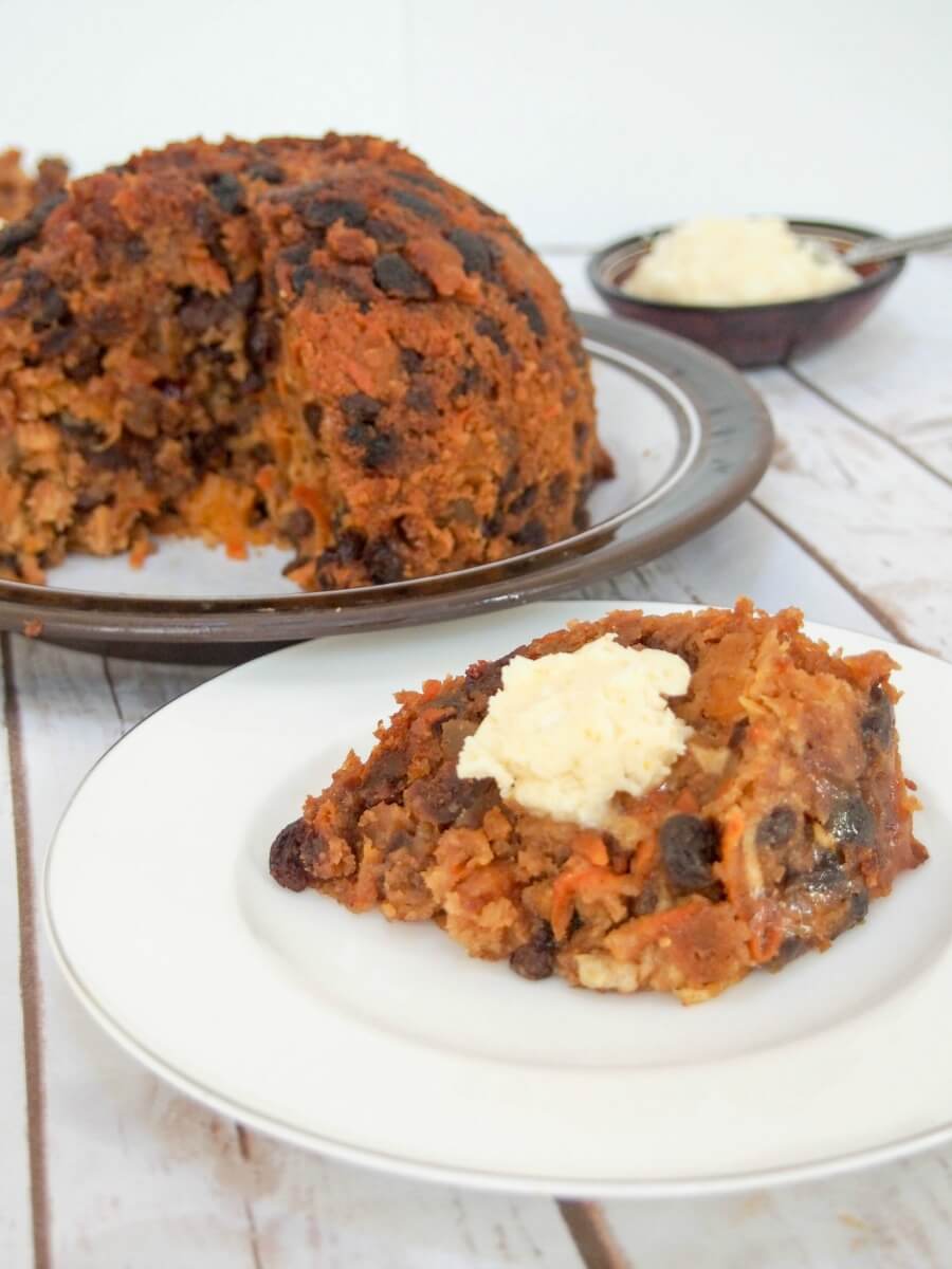 slice of lighter Christmas pudding with remaining pudding and brandy butter behind