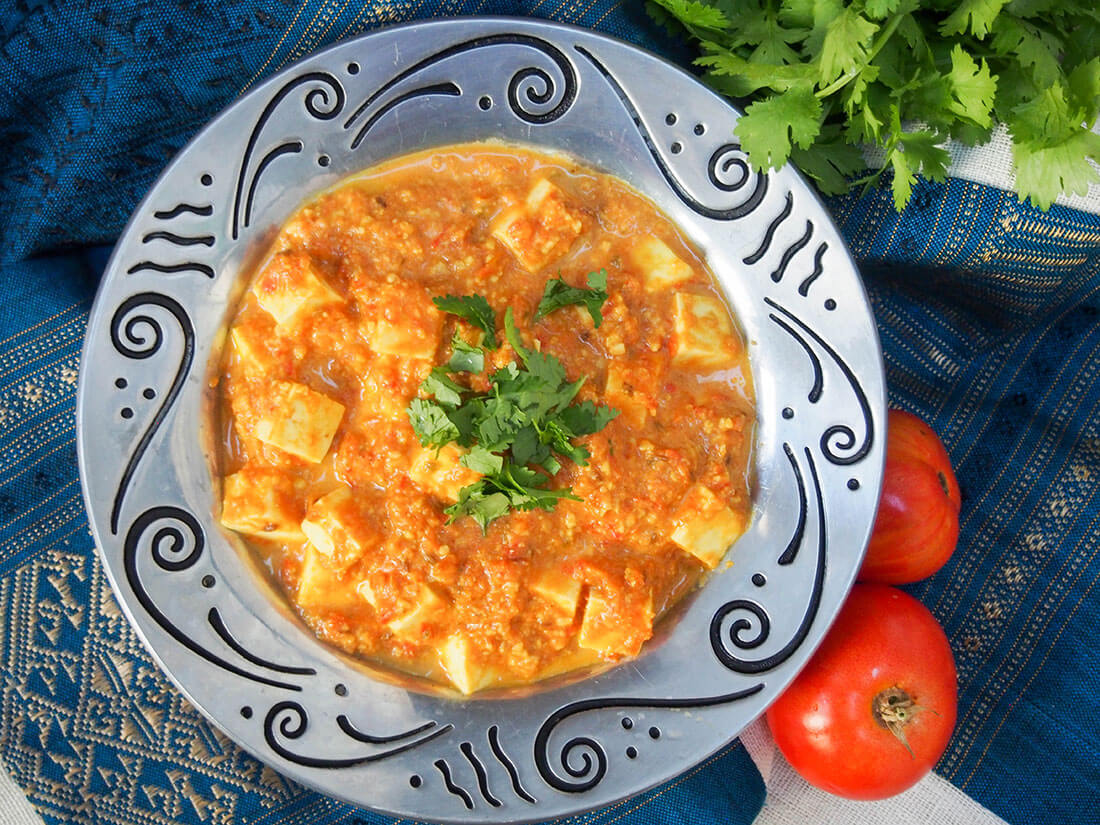 dish filled with paneer Makhani from overhead with tomatoes and cilantro bunch to side