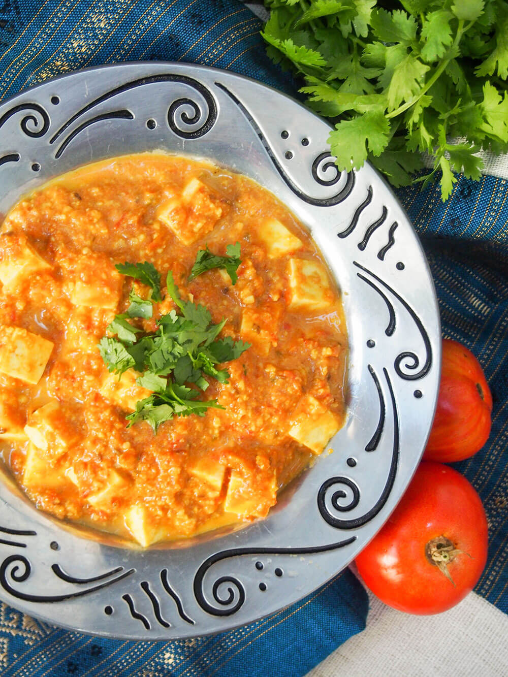 paneer Makhani in serving dish from overhead with cilantro and tomatoes to side