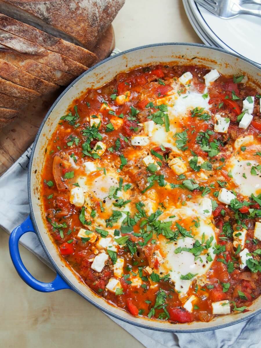 partial view of dish of beefed up shakshuka - shakshuka with meat - from overhead with bread in corner