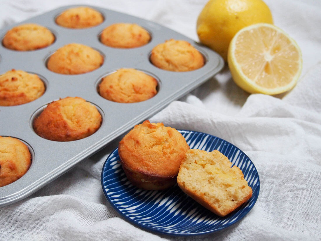mini lemon almond flour muffins in muffin tray with one split open on plate