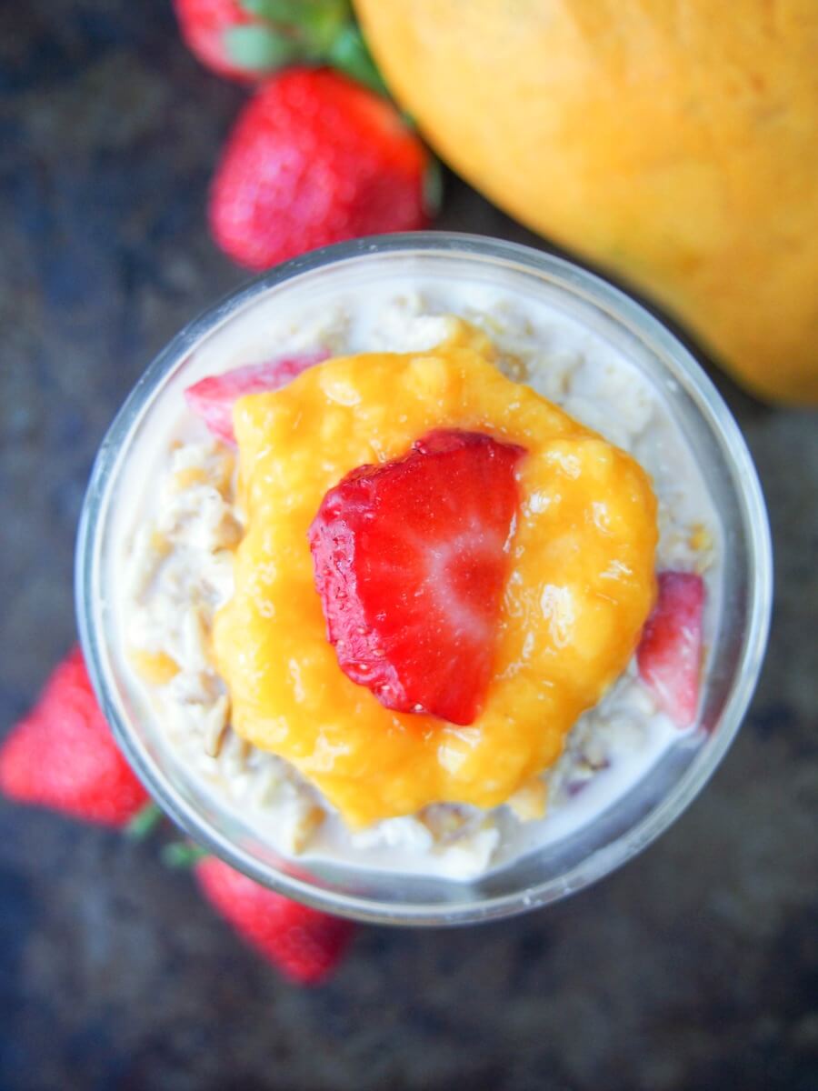 glass of mango and strawberry overnight oats from overhead with mango and strawberries to side