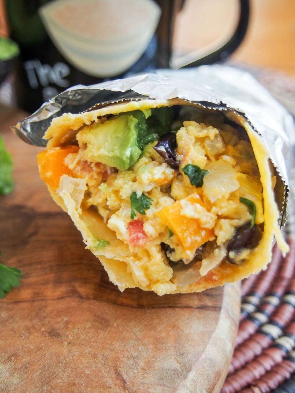 vegetarian breakfast burrito resting on wooden board with mug behind