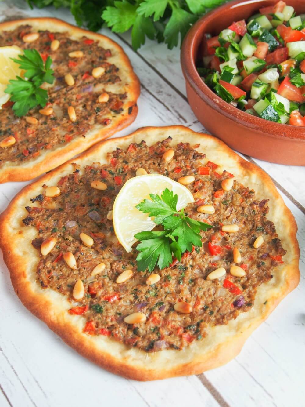 Lahmacun with a slice of lemon and sprig of parsley garnish on top with bowl of salad to side