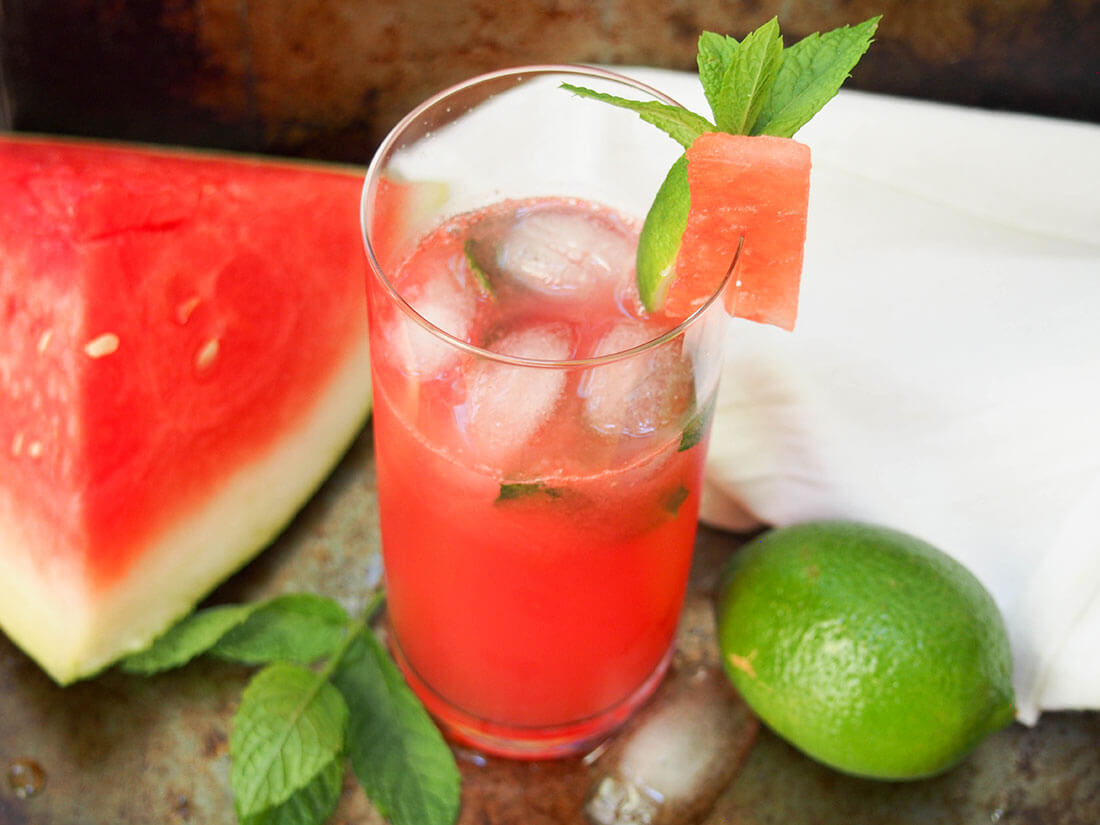 glass of watermelon mojito with watermelon slice to side