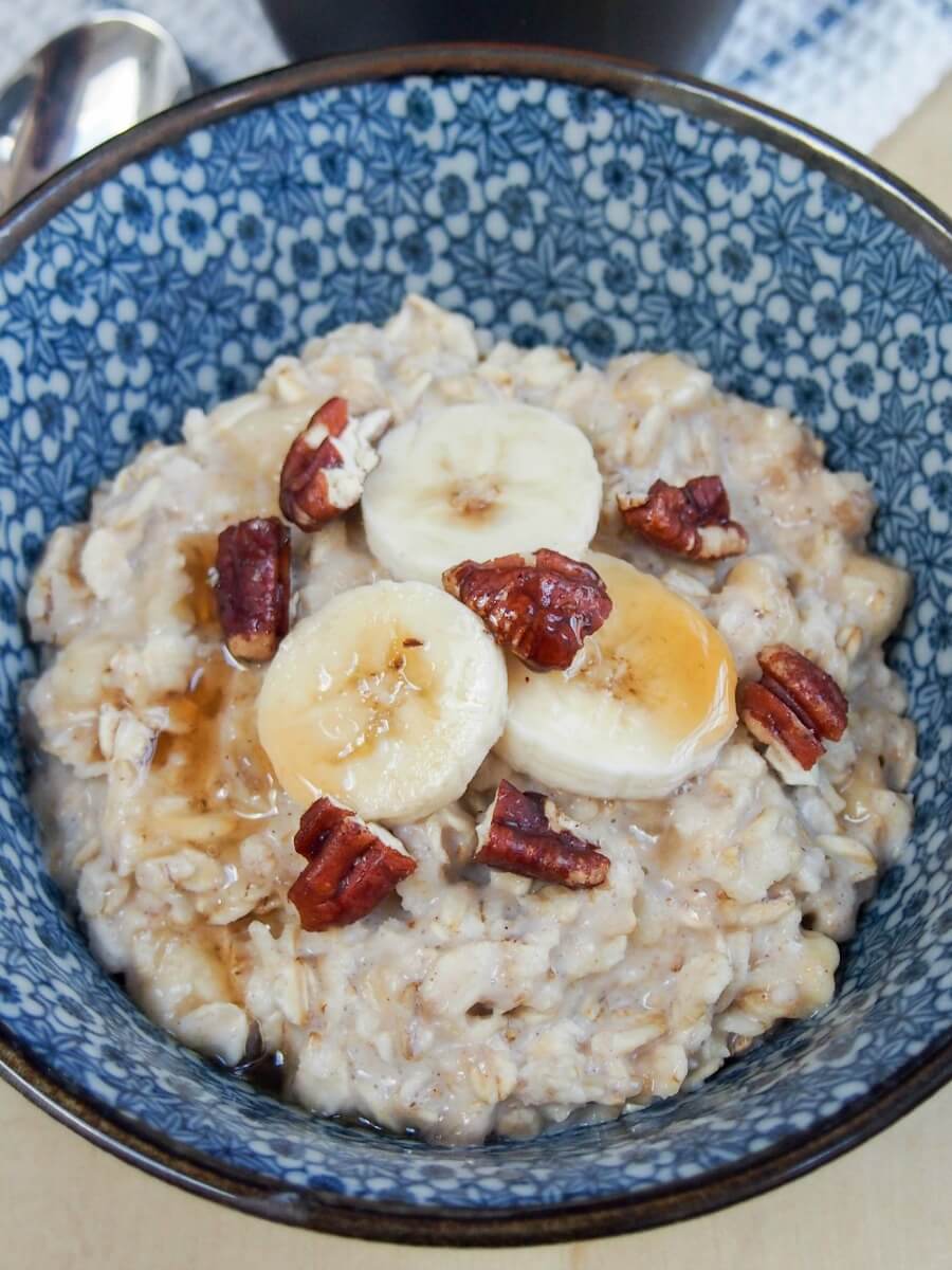 banana oatmeal close up in bowl with banana, pecans and syrup on top