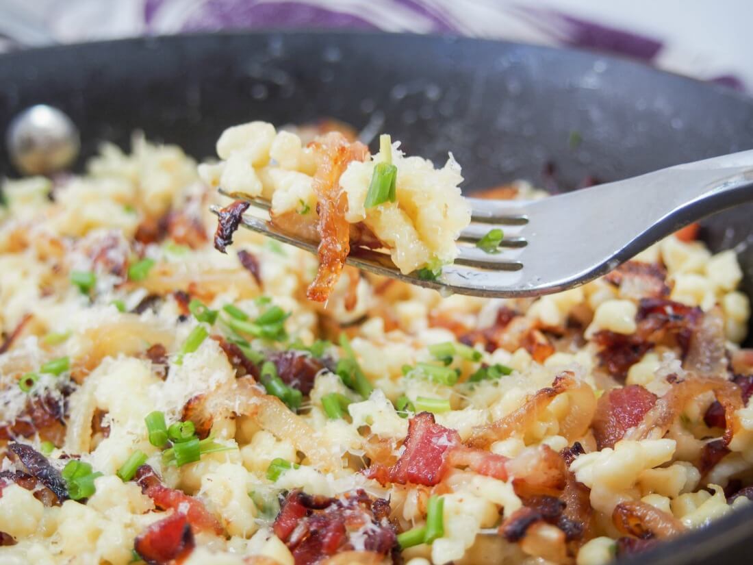 Taking forkful of bacon onion spaetzle from skillet