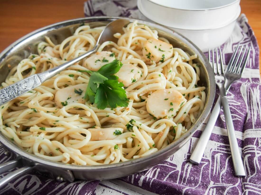 scallop pasta with garlic and white wine in skillet with forks to side