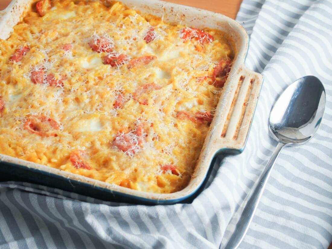 Cheesy orzo pasta bake in baking dish with spoon to side