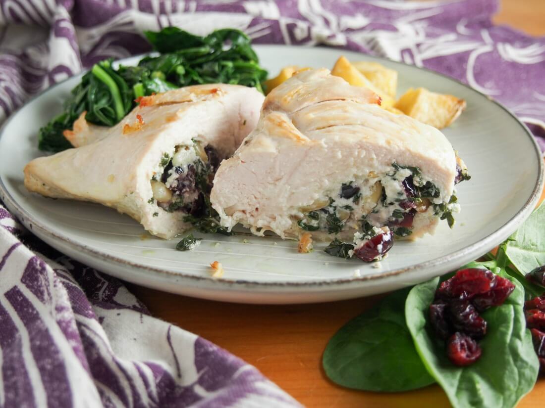 Goat cheese stuffed chicken with spinach and cranberries on plate with chicken cut open to see filling