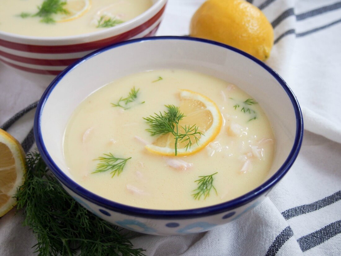 Bowl of avgolemono soup with lemon behind bowl