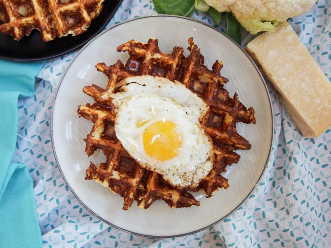 Cauliflower waffle on plate with egg on top and cheese block to side