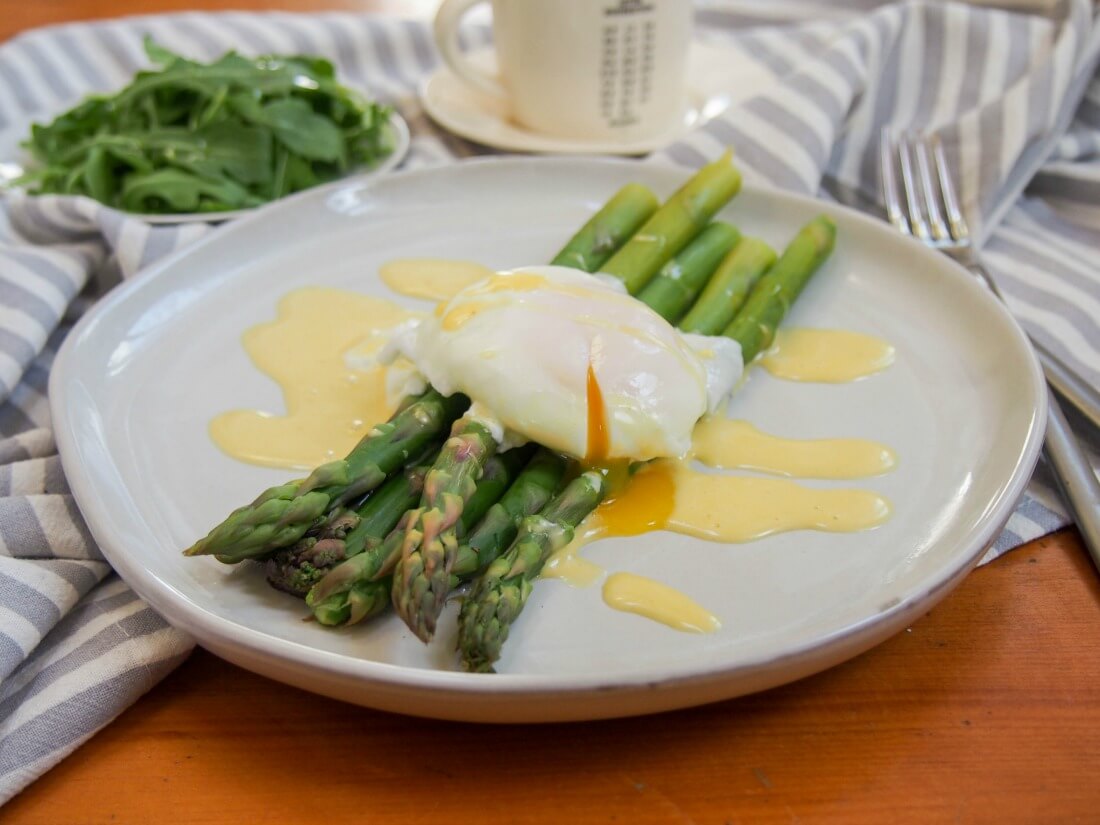 Asparagus with poached egg on top and Hollandaise sauce drizzled over with fork to side of plate