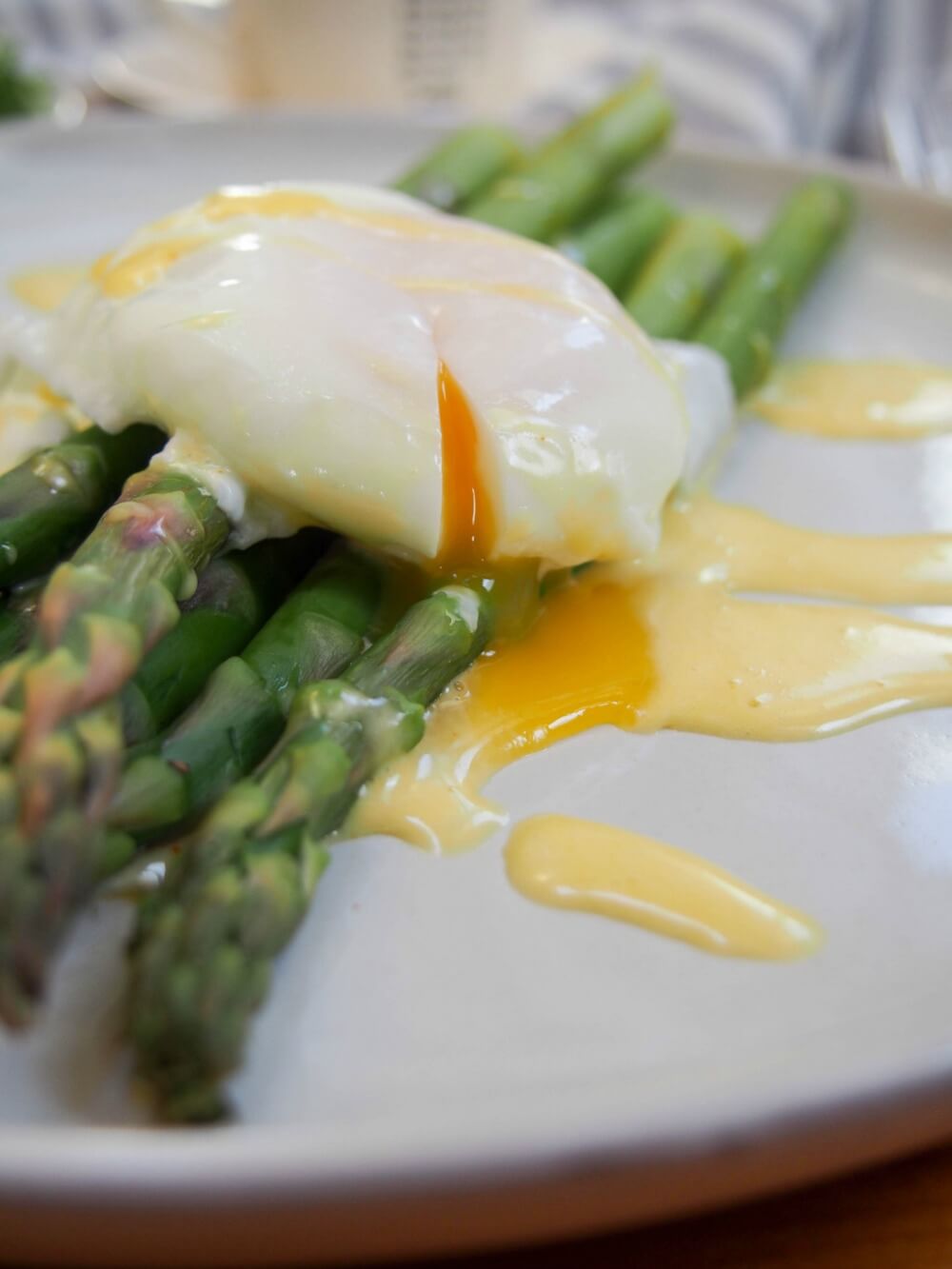 close up of poached egg on top of asparagus showing egg yolk cut and running into sauce