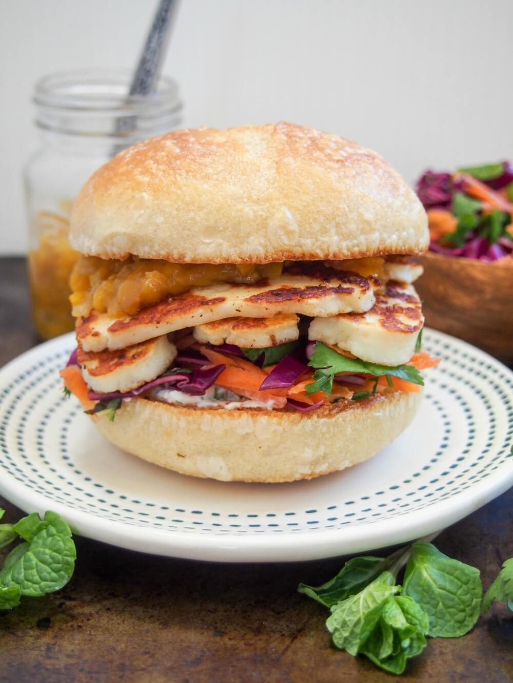 halloumi burger on plate showing slaw under and mango sauce on top of halloumi slices