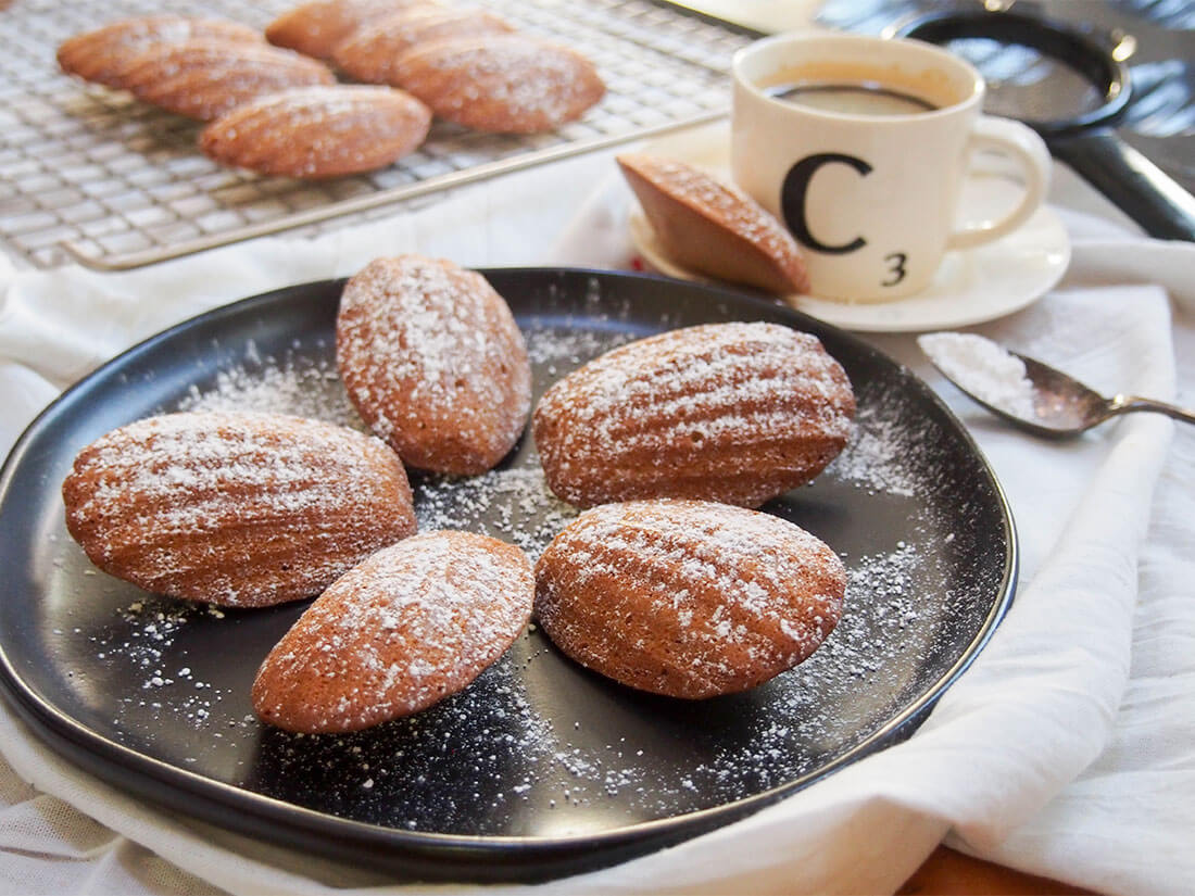 gingerbread madeleines on plate with coffee cup behind