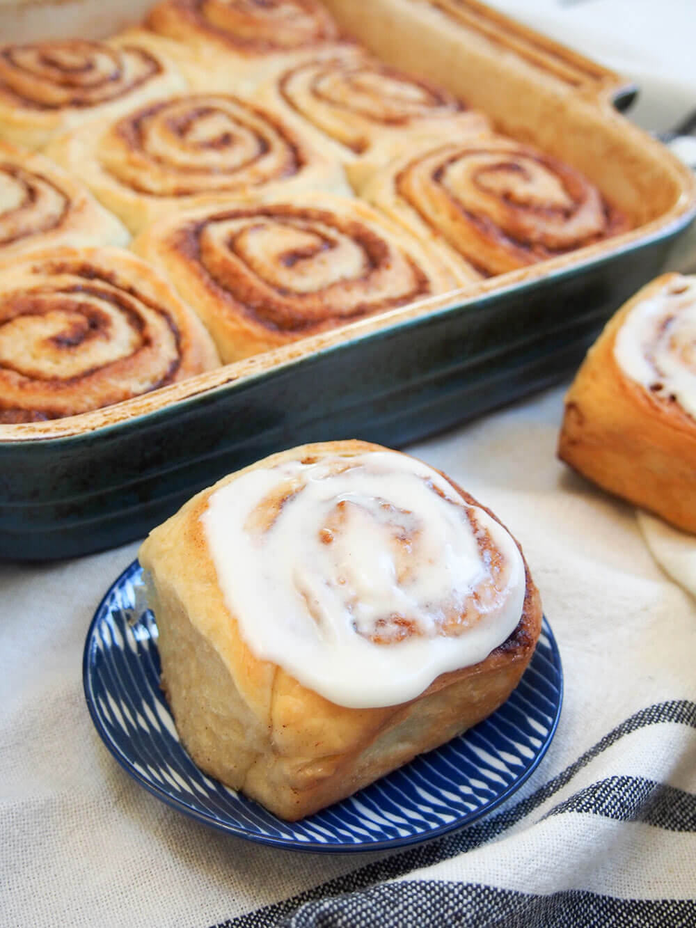 eggnog cinnamon roll with frosting sitting on small plate in front of dish with more rolls