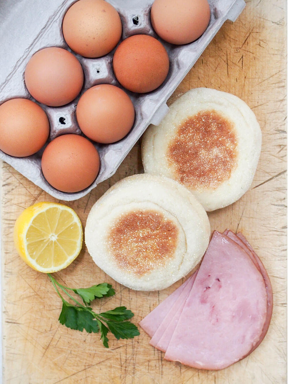eggs, muffins, ham, lemon and a little parsley laid out on cutting board