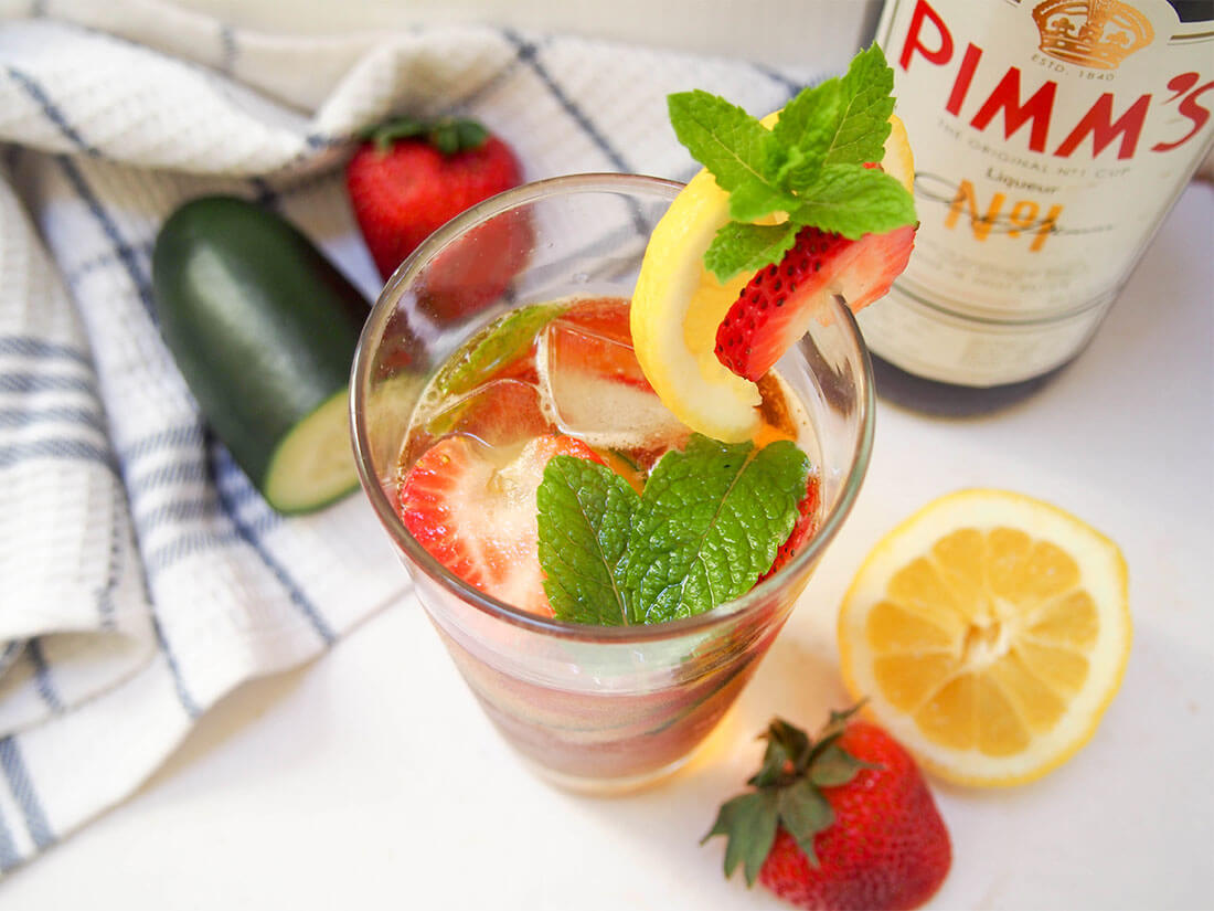 Pimm's cup cocktail with bottle and garnishes to side