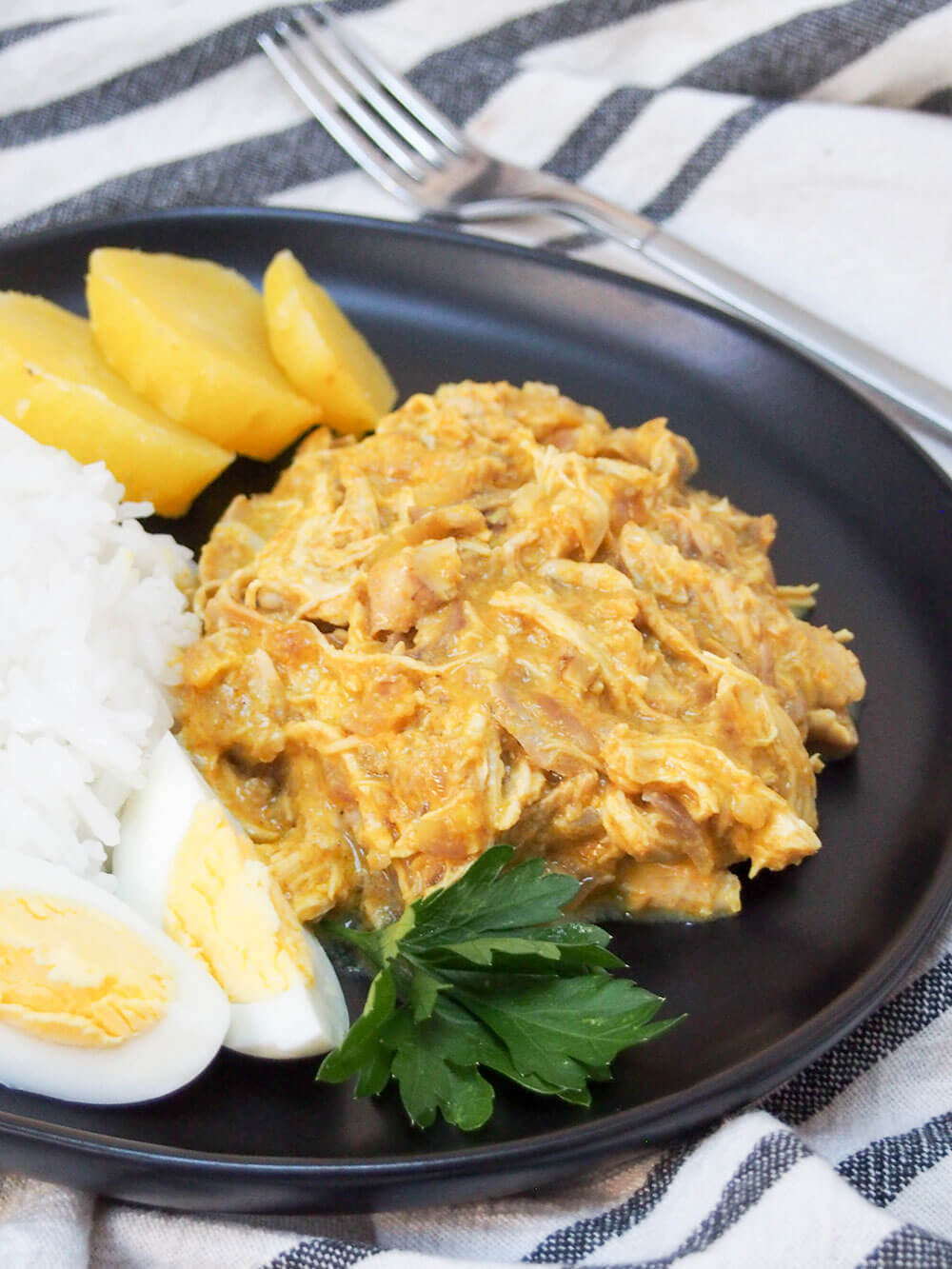 Aji de gallina (Peruvian chicken) served with traditional sides of rice, potato and egg with fork behind plate