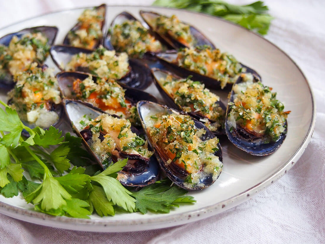 baked mussels on plate with parsley garnish to side