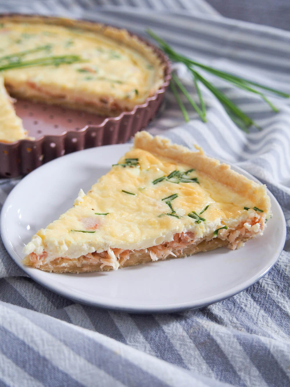 smoked salmon quiche with slice cut from it sitting in front on plate