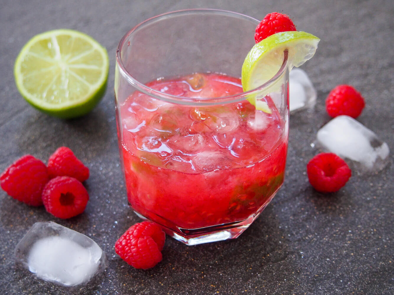 raspberry caipirinha in glass with raspberries and lime to side