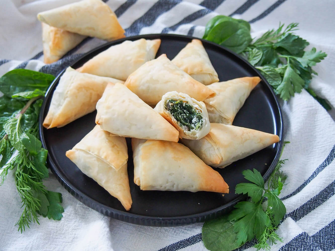 spanakopita triangles on plate with one bitten into, resting on others showing filling inside