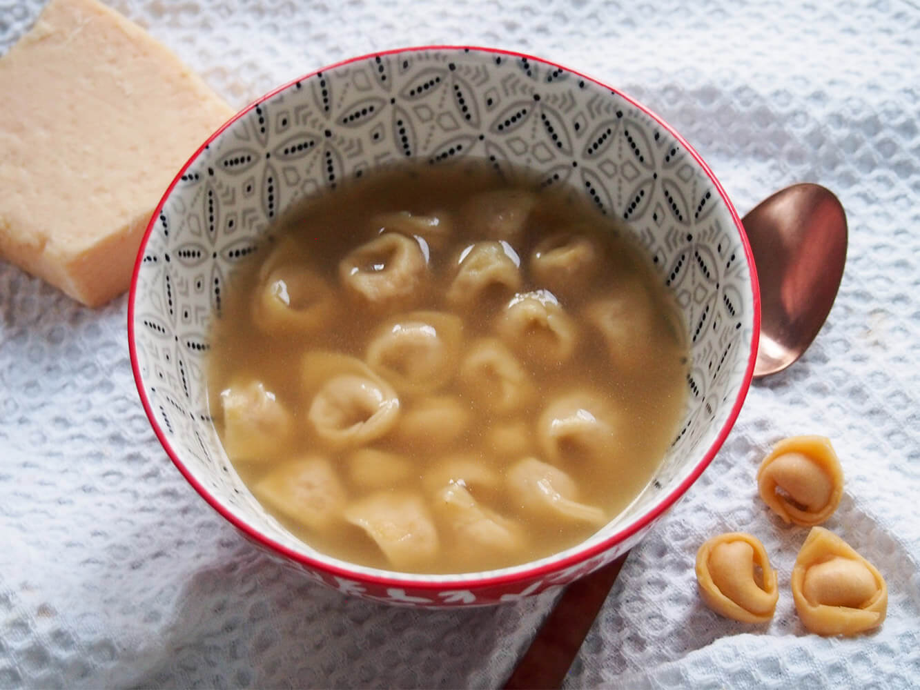bowl of tortellini in brodo with spoon and additional tortellini to side