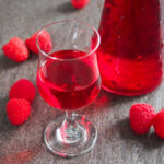 glass of raspberry liqueur with bottle behind and raspberries to side