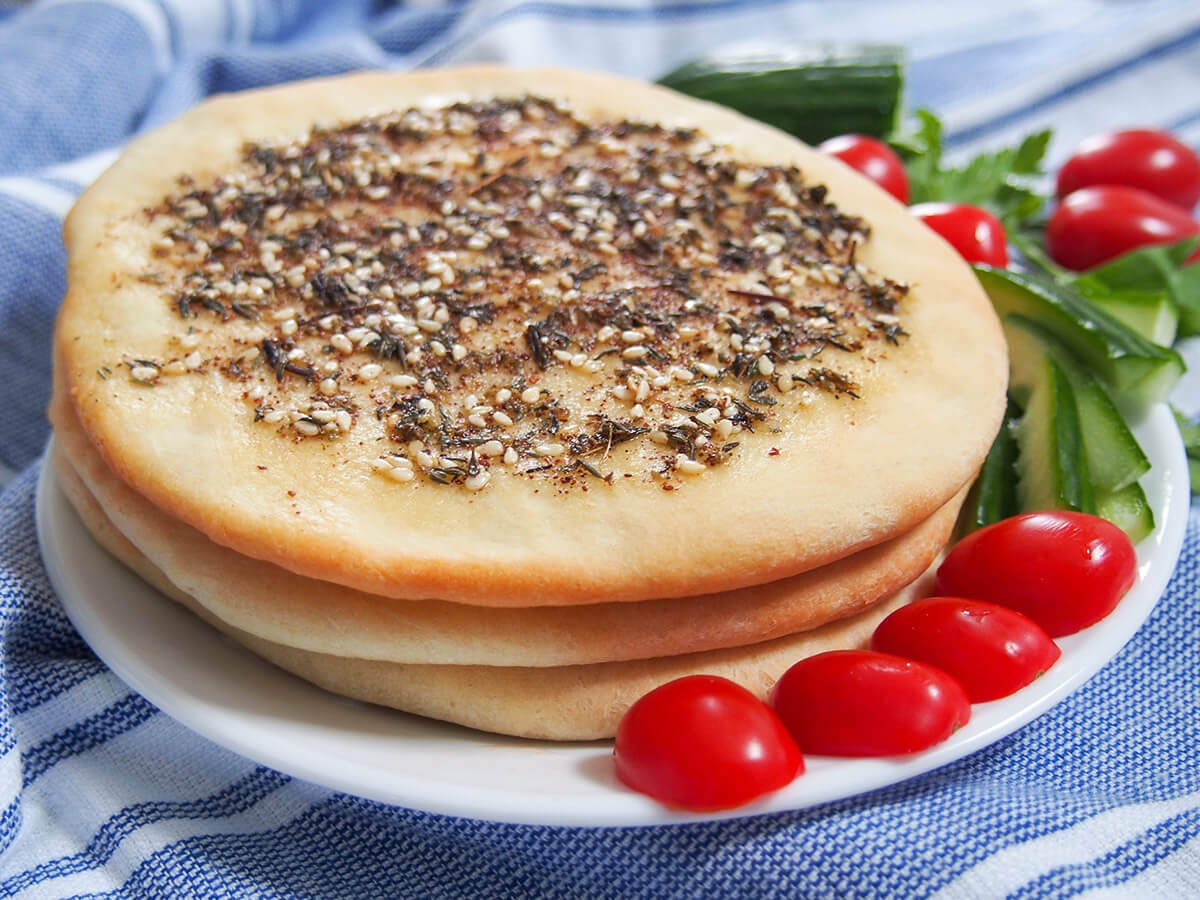 stack of Manakish Lebanese za'atar flatbread with tomatoes and cucumber to side of plate