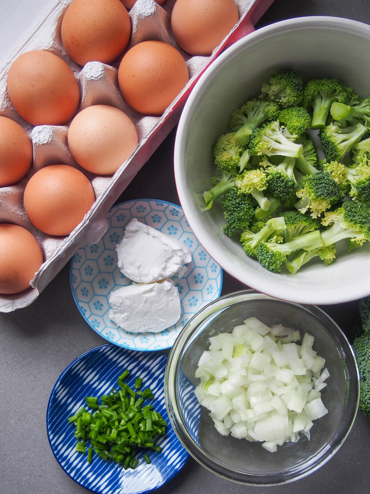tray of eggs, bowls with broccoli, goat cheese, chopped onion and chives