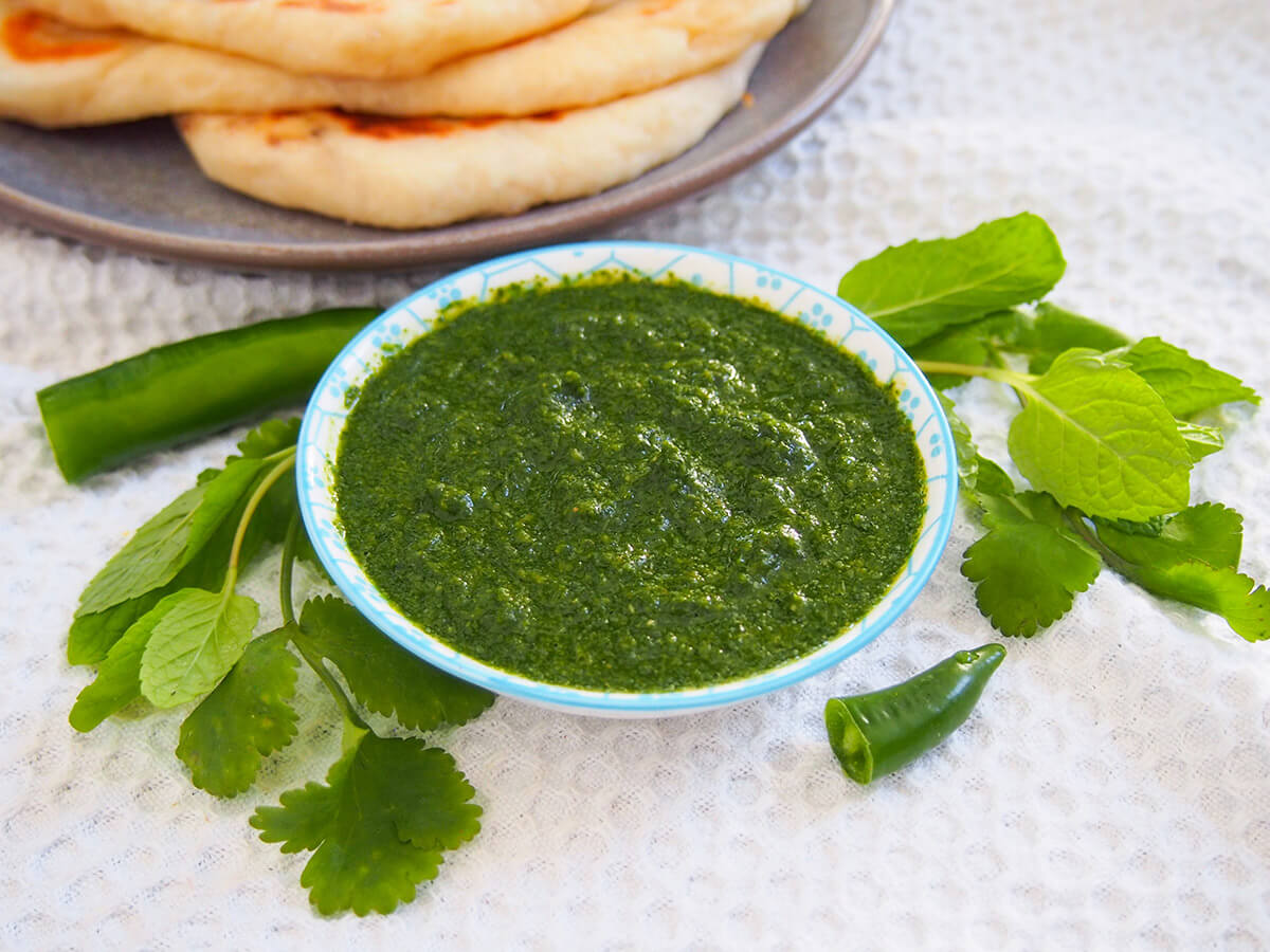 bowl of cilantro mint chutney with herbs and chili to side of bowl