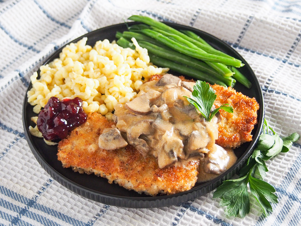 plate of jaegerschnitzel with spaetzle and beans behind