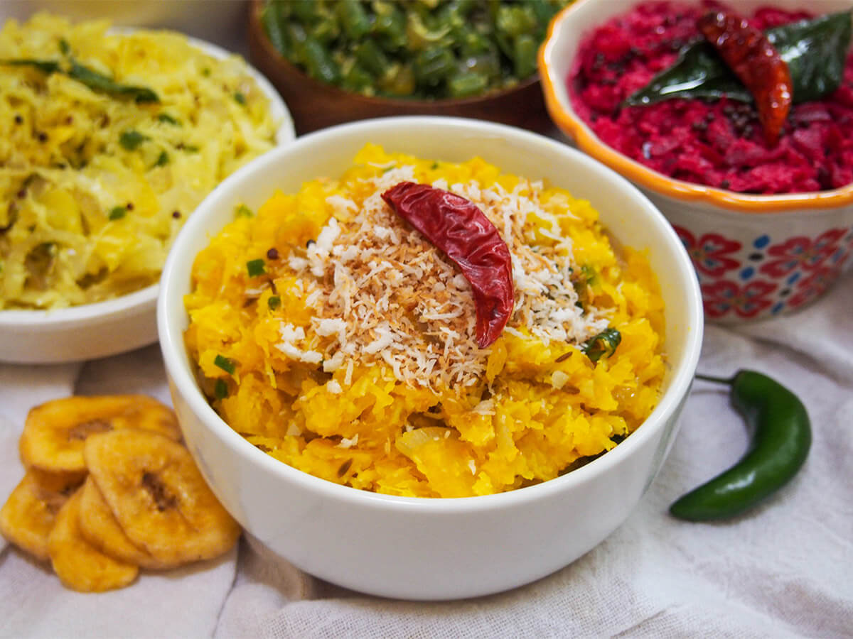bowl of pumpkin erissery with bowls of thorans and pachadi behind