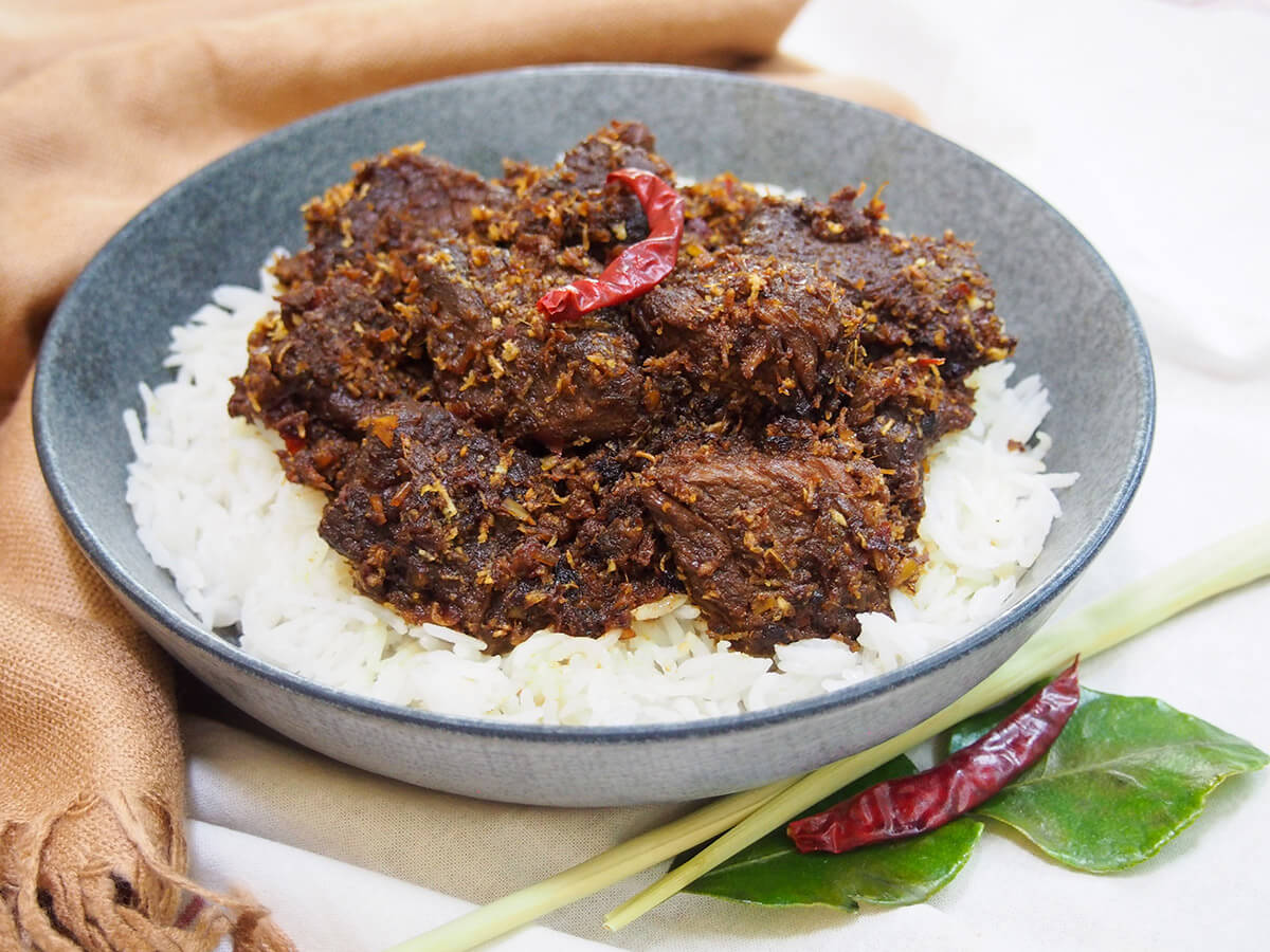 bowl of beef rendang over rice with spices below bowl