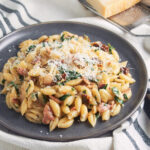 Bacon sun dried tomato pasta with spinach and cream on plate