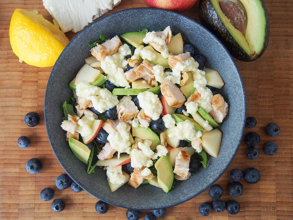 bowl of grilled chicken blueberry salad with blueberries around bowl and lemon and avocado above