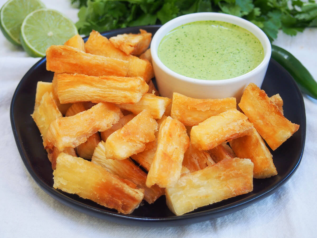 plate of yuca fries with bowl of Peruvian green sauce at the back and cut lime behind plate