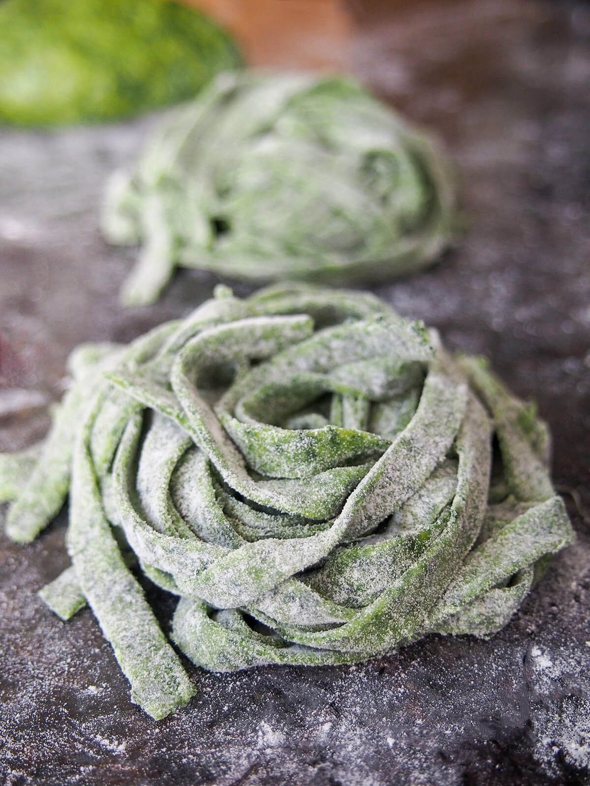 stacks of uncooked cut fresh spinach pasta dough cut in linguine, dusted with flour
