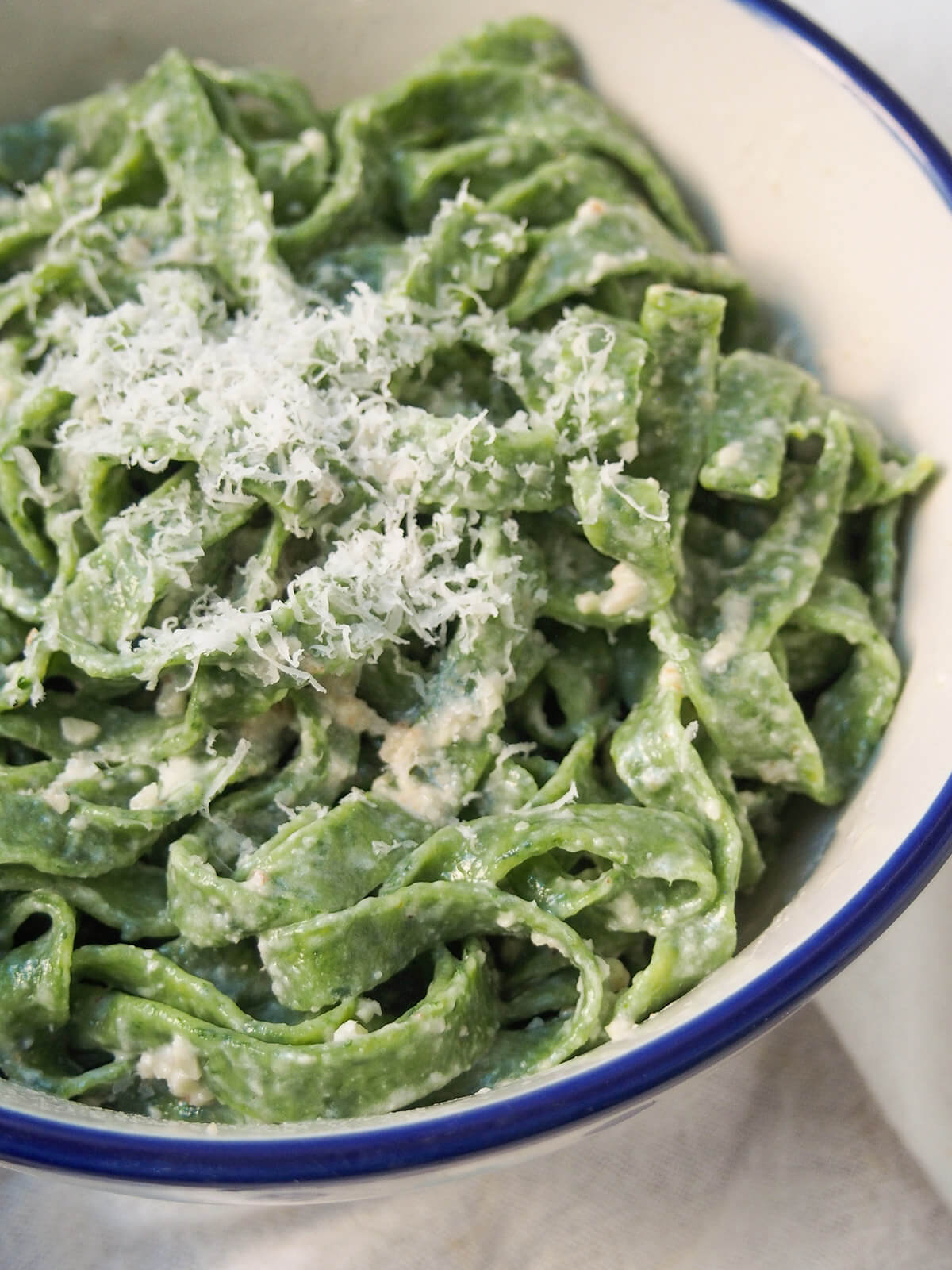 close up of fresh spinach pasta with walnut sauce topped with a little cheese