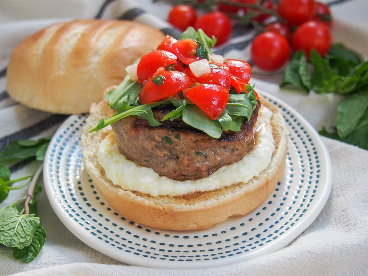lamb burger with feta sauce with top of bun behind plate