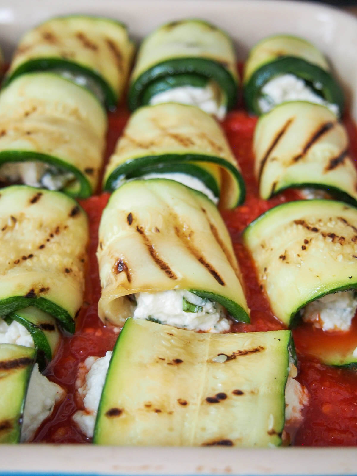 filled zucchini involtini rolls in dish with tomato marinara sauce before baking