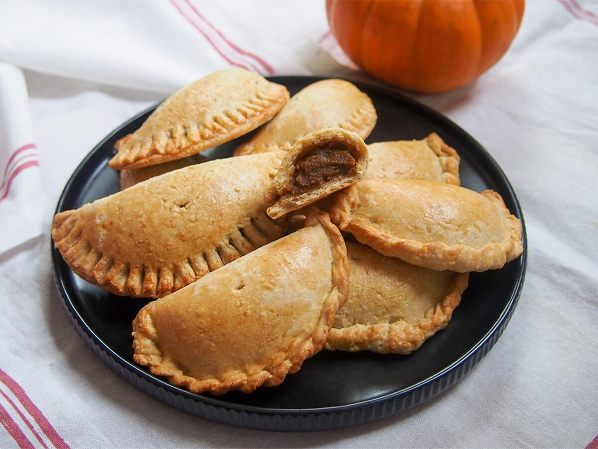 plate of pumpkin empanadas with a broken one on top showing filling
