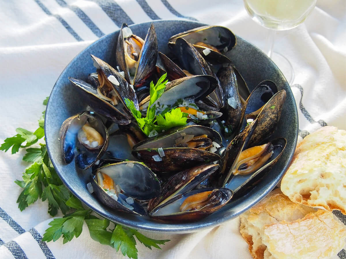 bowl of mussels in white wine with parsley around bowl and bread to one side