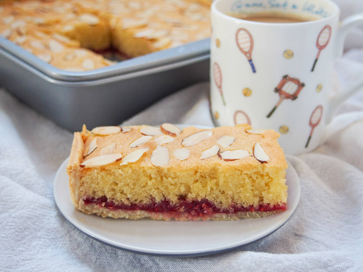 piece of Bakewell slice on plate with mug behind