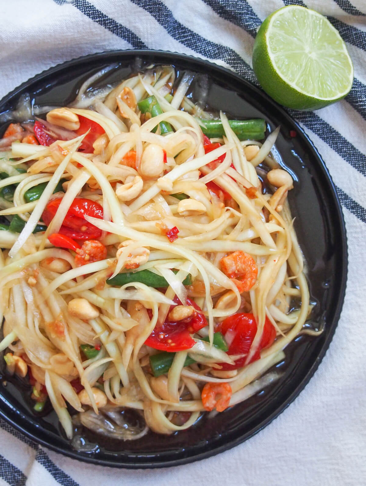 Thai green papaya salad is a classic Thai salad made with green papaya and a tasty dressing that has plenty of sour, sweet and spice flavor. It's easy to make, refreshing and delicious. plate of Thai green papaya salad with cut lime above plate