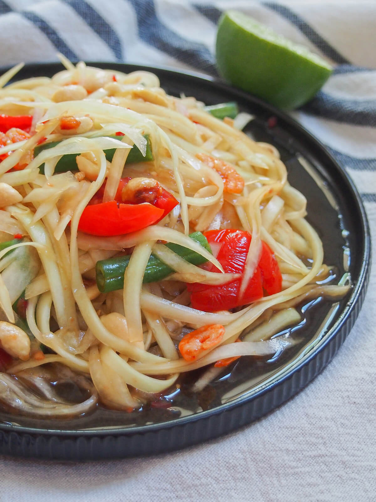 Thai green papaya salad is a classic Thai salad made with green papaya and a tasty dressing that has plenty of sour, sweet and spice flavor. It's easy to make, refreshing and delicious. partial side view of plate of Thai green papaya salad