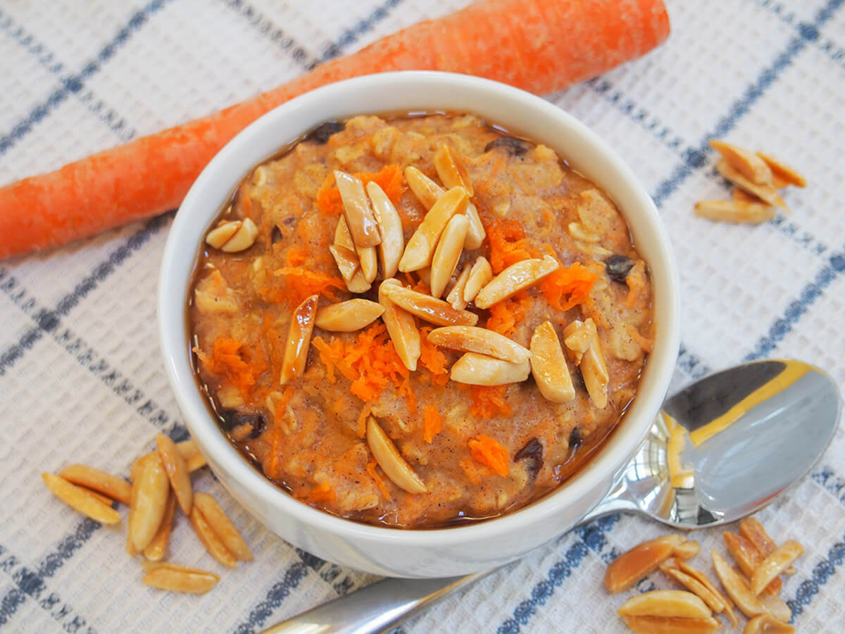 bowl of carrot cake oatmeal with spoon below bowl and carrot above