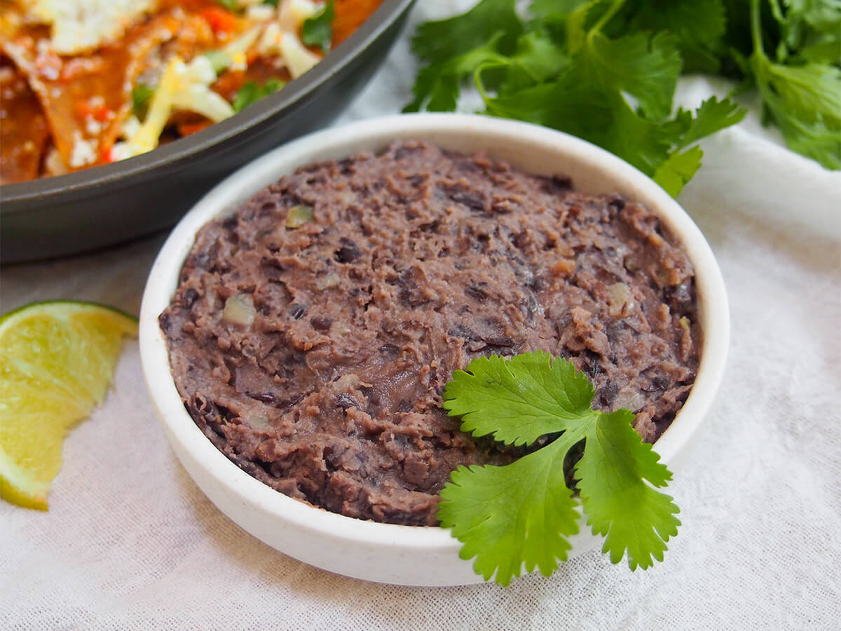 dish of refried black beans with cilantro and other food part in view behind